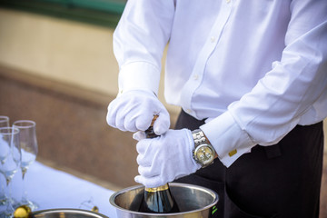 Hand of the waiter pours white wine in wineglass. Bright picture of pouring wine into glasses.