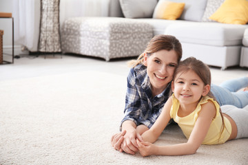 Cute little girl and her mother lying on cozy carpet at home