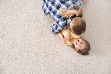 Cute little girl and her mother lying on cozy carpet at home