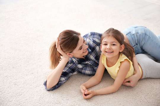 Cute little girl and her mother lying on cozy carpet at home
