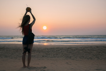 Fototapeta premium A woman with a coconut looks at the sunset