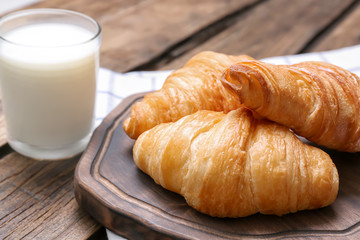 Wooden board with tasty croissants and glass of milk on table