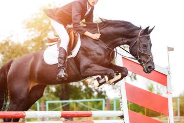 Foto op Canvas Jonge ruiter man springt op paard over obstakel op springconcours © skumer