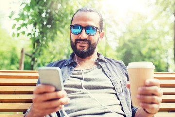 people, music, technology, leisure and lifestyle - man with earphones and smartphone drinking...