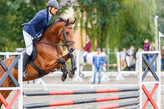 Young rider man jumping on horse over obstacle on show jumping competition
