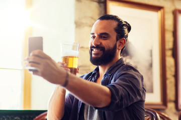 people and technology concept - man with smartphone drinking beer and taking selfie at bar or pub