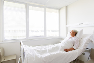 medicine, healthcare and old people concept - sad senior woman lying on bed at hospital ward - obrazy, fototapety, plakaty