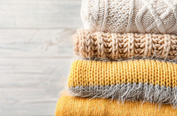 Stack of warm knitted clothes on light background