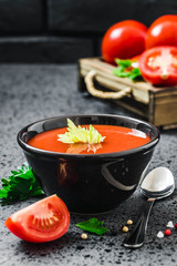 Roasted tomato soup in a bowl and fresh tomatoes in wooden box on dark concrete background. Selective focus, space for text.