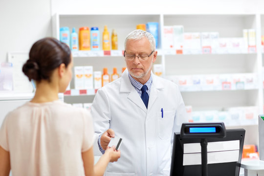 medicine, healthcare and people concept - senior apothecary taking credit card from customer at pharmacy cash register