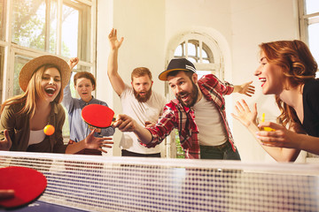 Group of happy young friends playing ping pong table tennis - obrazy, fototapety, plakaty