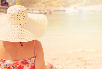 Young woman in summer dress and hat standing on sand and looking to a the port of Porto Vromi, Greece.