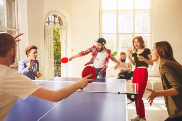 Group of happy young friends playing ping pong table tennis
