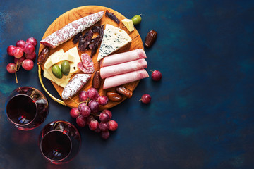 Red wine in glasses, appetizer, grapes, cold meat, cheese with mildew. Delicatessen snacks on a blue background. Top view, copy space.