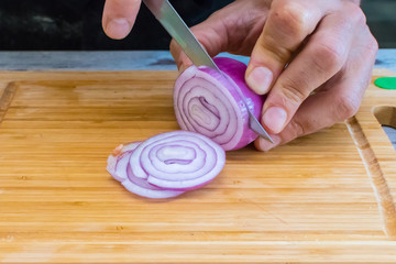  A man is cutting onion on a wooden chopping board 