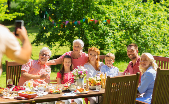 leisure, holidays and people concept - happy family having festive dinner or summer garden party and photographing by smartphone
