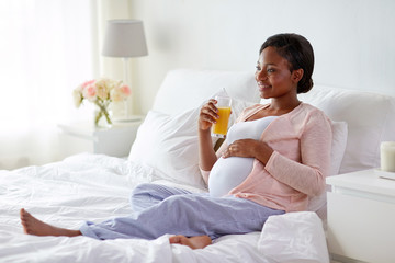 Obraz na płótnie Canvas pregnancy, people and rest concept - happy pregnant african american woman drinking orange juice in bed at home