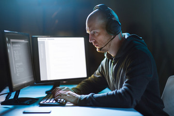 cybercrime, hacking and technology concept - male hacker with headset and coding on computer screen...