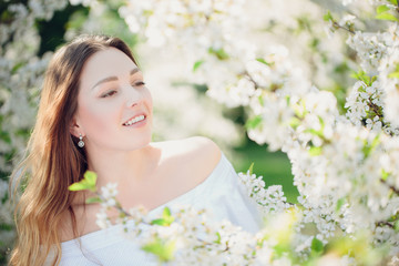 Young beautiful blonde woman in blooming almonds garden.