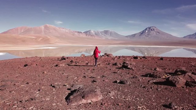Hiker woman using hiking sticks to climb the hill. Aerial view of mountain lake panorama in the Atacama desert. 