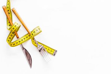 Diet, weight loss, slimming concept. Fork and knife with wound measuring tape on white background...