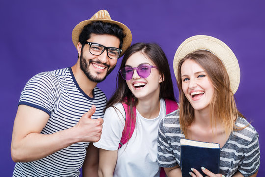 Happy smiling students dressed in t-shirts and hats and eyeglasses before purple background