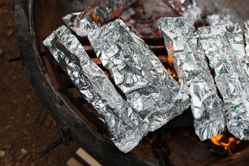 Camping meals prepared in foil cook over a campfire