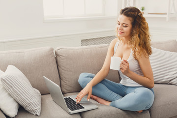 Obraz premium Young girl with laptop sitting on beige couch