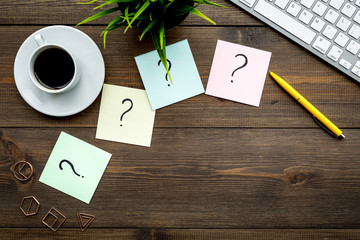 Question mark on sticky notes on office desk on dark wooden background top view copy space. FAQ...