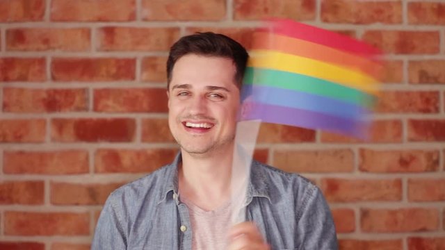 Young man with rainbow flag on brickwall background