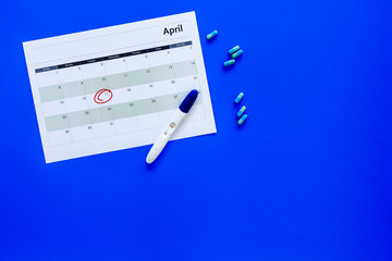 Planning pregnancy. Positive pregnancy test near calendar page and pills on blue background top view copy space