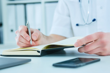 Fototapeta premium Male doctor or medical student holding ballpoint pen and writing on notepad. Therapist fills the patient admission schedule