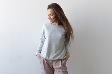 Beautiful woman in gray sweatshirt stands on white background. Mock-up.