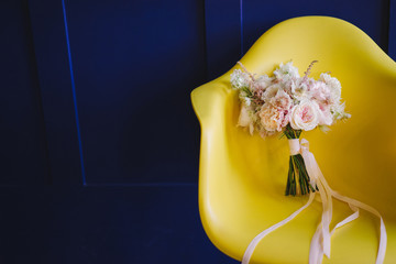 Bridal morning details. Wedding bouquet of white, beige and pink flowers with on a yellow chair. Blue background, bright colors, contrast composition.