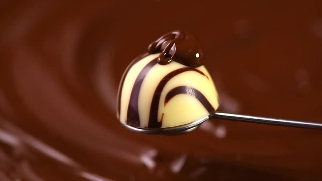 Melted chocolate pouring on praline candy closeup. White chocolate truffle candy covered dark chocolate on brown. Dessert. Slow motion 4K UHD video 3840X2160
