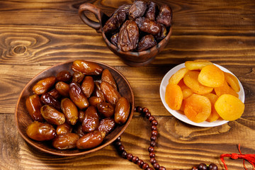 Dried apricots and dates fruit with wooden rosary on wooden table
