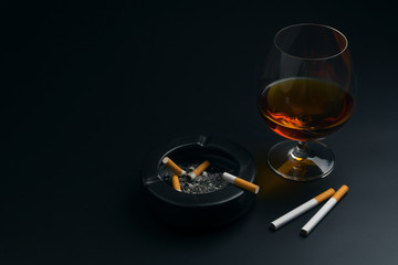 a glass of brandy, cigarettes and black ceramic ashtray full of ashes with the cigarette butt, on...