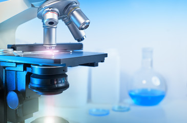 Scientific background with closeup on light microscope and laboratory out of focus