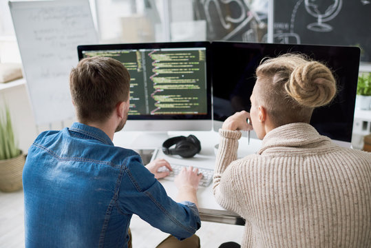 Back view portrait of two contemporary program developers writing code sitting at desk with computer and collaborating on startup project in modern office, copy space