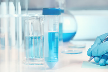 Biological or biochemical lab out of focus, closeup on gloved hand writing a note