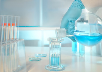 Biological or biochemical lab out of focus, closeup on gloved hand holding flask