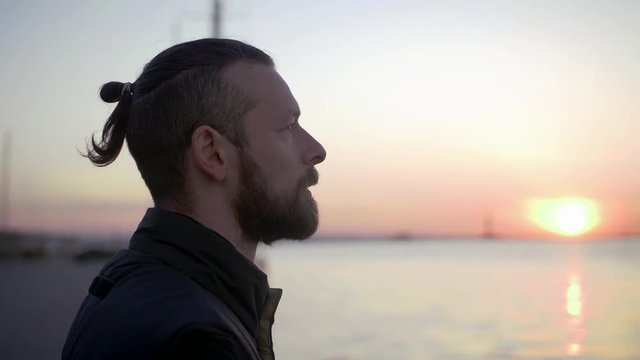 Portrait of stylish hipster man on sea port background during sunset, looking aside
