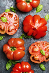 Big red tomatoes with green basil leaves on the old stone table, top view