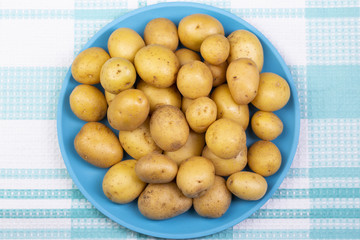 Fresh potatoes lie on a plate of turquoise color. The background is a white and turquoise tablecloth. Top view.
