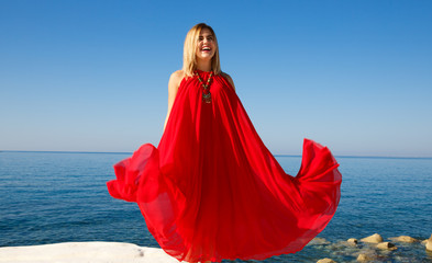 Woman in the red dress on the white stone at the beach in Cyprus.