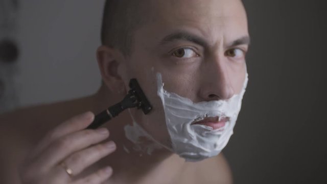 Man shaving with foam and manual razer. Close up of man shaving beard.