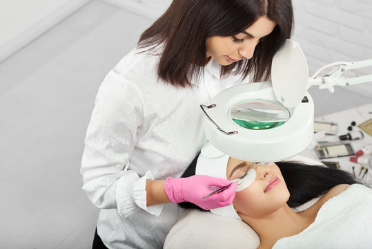 Professional lashmaker working with a client in beaty salon. Woman lying on cosmetologiacal coach during lashes enlarging. woman with pretty face wearing headbandage and stickers for lashmaking .