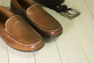 Mens moccasin shoes and belt on a wooden background