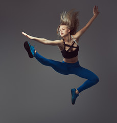 Fototapeta premium Young ballerina in sportswear dances and jumps in a studio. Isolated on a gray background.