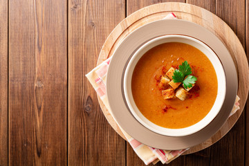 Red lentil cream soup with croutons in bowl on wooden table